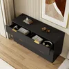A black sideboard with gold accents, drawers open to reveal items like books, a camera, and headphones, set in a room with wood flooring and a curtain. Produktbild-Vorschau