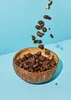 Chocolate-covered peanuts falling into a coconut bowl. Produktbild-Vorschau
