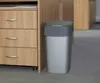 A silver trash can with a gray lid sits next to a wooden filing cabinet on a gray carpeted floor. Anteprima dell’immagine prodotto