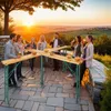 People enjoying drinks and snacks at a standing table outdoors during sunset. Produktbild-Vorschau