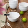 A stack of white ceramic bowls on a wooden table, with limes and a spoon. Produktbild-Vorschau