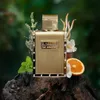 A gold perfume bottle is displayed on a piece of wood, surrounded by natural elements like mint leaves, an orange slice, and dried plants. Podgląd zdjęcia produktu