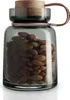 A glass storage jar filled with almonds, with a wooden lid and a leather handle. Voir les images du produit