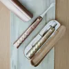 Two rose gold and gold electric toothbrushes are displayed on a marble surface with a wooden background. Náhled obrázku produktu