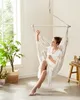 A woman relaxing in a hanging chair indoors, with a plant and a stool nearby. Náhled obrázku produktu