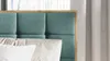A close-up view of a bed with a teal upholstered headboard and pillows. Náhled obrázku produktu