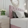 A close-up view of a pink upholstered bed with pillows and a nightstand with tulips. Produktbild-Vorschau