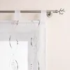 A close-up view of a white sheer curtain with embroidered brown wavy lines and small beads, hanging from a metal curtain rod. Produktbild-Vorschau