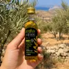 Hand hält Physis of Crete Olivenöl Flasche im Olivenhain Produktbild-Vorschau