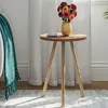 A small wooden side table with a vase of flowers and a phone on it, next to a couch with a teal blanket. Produktbild-Vorschau