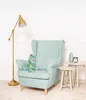 A plush dinosaur toy sits on a light blue armchair next to two small side tables, a floor lamp, and a white wall. Produktbild-Vorschau