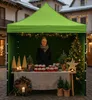 A woman stands behind a market stall selling jars of jam, decorated for Christmas. Voir les images du produit