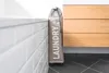 A laundry basket is placed next to a bathtub and a wooden cabinet in a bathroom. Anteprima dell’immagine prodotto