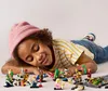 A young girl is lying on the floor surrounded by LEGO minifigures. Produktbild-Vorschau