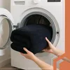 Hands placing a folded black blanket into a washing machine. Náhľad obrázku produktu