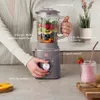 A person is using a taupe stand mixer to make a smoothie, with ingredients in the blender jar and a finished smoothie in a glass. Voir les images du produit