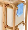A close-up view of a bamboo laundry basket with two fabric bins and a blue towel hanging on the side. Podgląd zdjęcia produktu