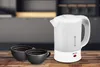 A white electric kettle and two black coffee cups are placed on a wooden table in a kitchen setting. Voir les images du produit