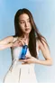 A woman holding a blue bottle of product against a light blue background. Produktbild-Vorschau