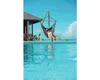 A woman relaxing in a hammock chair next to a swimming pool with a view of the ocean. Produktbild-Vorschau
