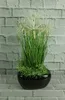 A black ceramic pot with artificial grass and white flowers against a brick wall. Produktbild-Vorschau
