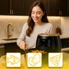 A woman is smiling while using a black and gold air fryer in a kitchen. There are icons of food items below the air fryer. Produktbild-Vorschau