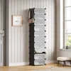 A tall, black shoe rack with clear plastic doors is shown in a room with white paneled walls and a doorway on the left. A framed picture hangs on the wall, and a handbag and bottle are hanging from hooks on top of the shoe rack. A small bench and slippers  Voir les images du produit