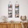A wall decorated with hanging photo frames above a wooden cabinet with books and a lamp. Produktbild-Vorschau