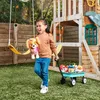 A young girl is playing with stuffed animals in a backyard with a swing set and a wagon. Produktbild-Vorschau