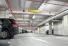 An interior view of a parking garage with cars parked and overhead lighting and pipes. Podgląd zdjęcia produktu