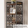 A close-up of a tall, narrow corner bookshelf with wooden shelves and black metal frame. The shelves are decorated with floral metal accents. There are framed pictures and a decorative piece on the shelves. Text overlay at the bottom right. Podgląd zdjęcia produktu