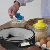 A person is using a digital kitchen scale with a bowl to measure sugar. There are also jars of sugar and eggs in the background. Produktbild-Vorschau