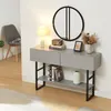 A modern console table with drawers and a shelf, decorated with a lamp, books, a radio, a framed picture, and dried flowers, placed against a white wall with a round mirror above it. A chair is visible in the background. Anteprima dell’immagine prodotto
