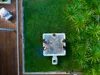 An aerial view of a hot tub with people in it, surrounded by grass and plants, next to a wooden deck. Náhled obrázku produktu