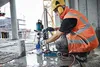 A construction worker is using a core drill machine on a concrete floor. Voir les images du produit