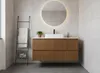 A modern bathroom vanity with a wooden finish, a white rectangular sink, and a black faucet, set against tiled walls with a backlit round mirror above. A black ladder towel rack with white towels is to the left, and a small potted plant sits on the counter Produktbild-Vorschau
