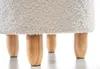 A close-up view of the bottom part of a white, fluffy ottoman, showing its four wooden legs. Produktbild-Vorschau