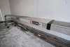A long, silver plank is supported by green ladder-like legs, resting against a white wall in what appears to be a construction or workshop environment. Produktbild-Vorschau