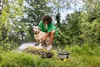 A woman is washing a dog outdoors in a grassy area with trees in the background. Produktbild-Vorschau