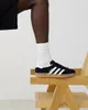 A person's leg wearing an Adidas sneaker is resting on a wooden chair. Produktbild-Vorschau