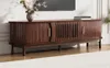 A brown TV stand with slatted doors and gold handles is shown in a room with a TV above it. Produktbild-Vorschau