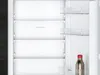 The interior of an open refrigerator with multiple shelves and a bottle on the bottom shelf. Produktbild-Vorschau