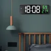 A digital clock mounted on a wall above a bed. Voir les images du produit