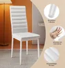 A white dining chair is shown in a room setting with a lamp and a wall. Náhled obrázku produktu