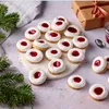 A collection of Christmas cookies with jam in the center, arranged on a white marble platter, with a Christmas tree branch and a gift box in the background. Produktbild-Vorschau