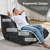 A woman is relaxing on a dark gray bean bag chair in a living room setting. Produktbild-Vorschau