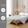 A bed with a light gray quilted blanket laid out, with a side table and a plant next to it. The left side of the image shows available sizes. Produktbild-Vorschau