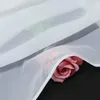 A close-up of white sheer fabric with a pink rose peeking out from underneath. Produktbild-Vorschau