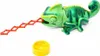 A green toy chameleon with its tongue extended, next to a yellow bowl, on a white background. Anteprima dell’immagine prodotto