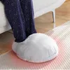 A person's legs are shown wearing navy blue pajamas with white stars, with their feet inside a large, plush gray foot warmer. The scene is set indoors, likely in a living room, with a couch and a rug visible. Produktbild-Vorschau